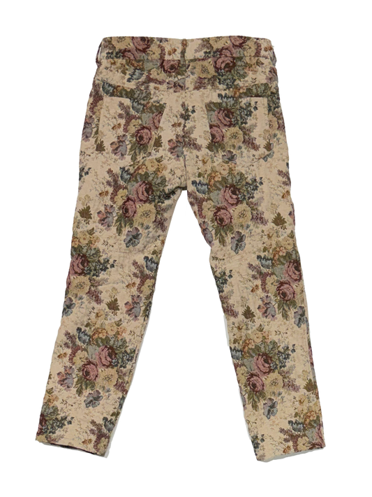 A pair of cropped pants featuring a vintage floral tapestry pattern in muted tones of pink, green, and brown on a beige background.